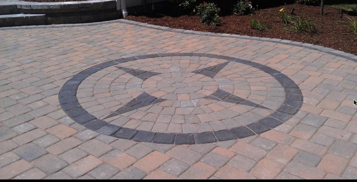A finished paver patio with a compass star medallion, a stone seat wall and rose beds