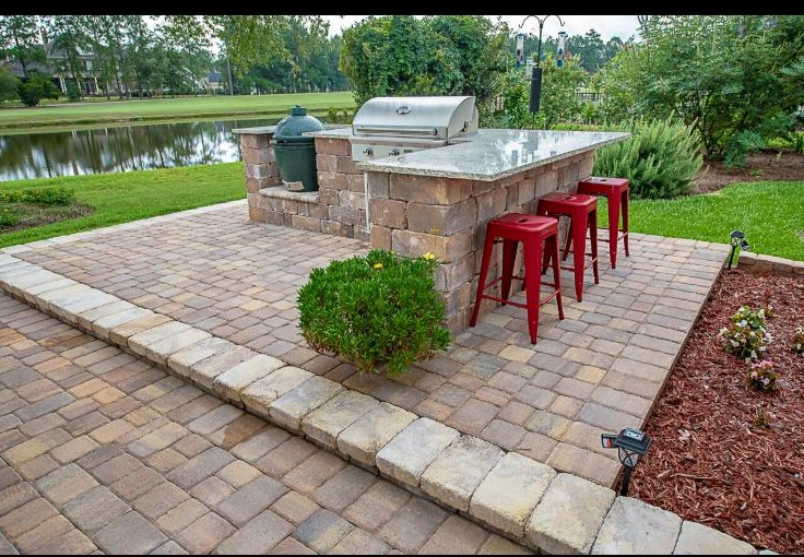 A custom paver patio with a built in stone outdoor kitchen beside the water